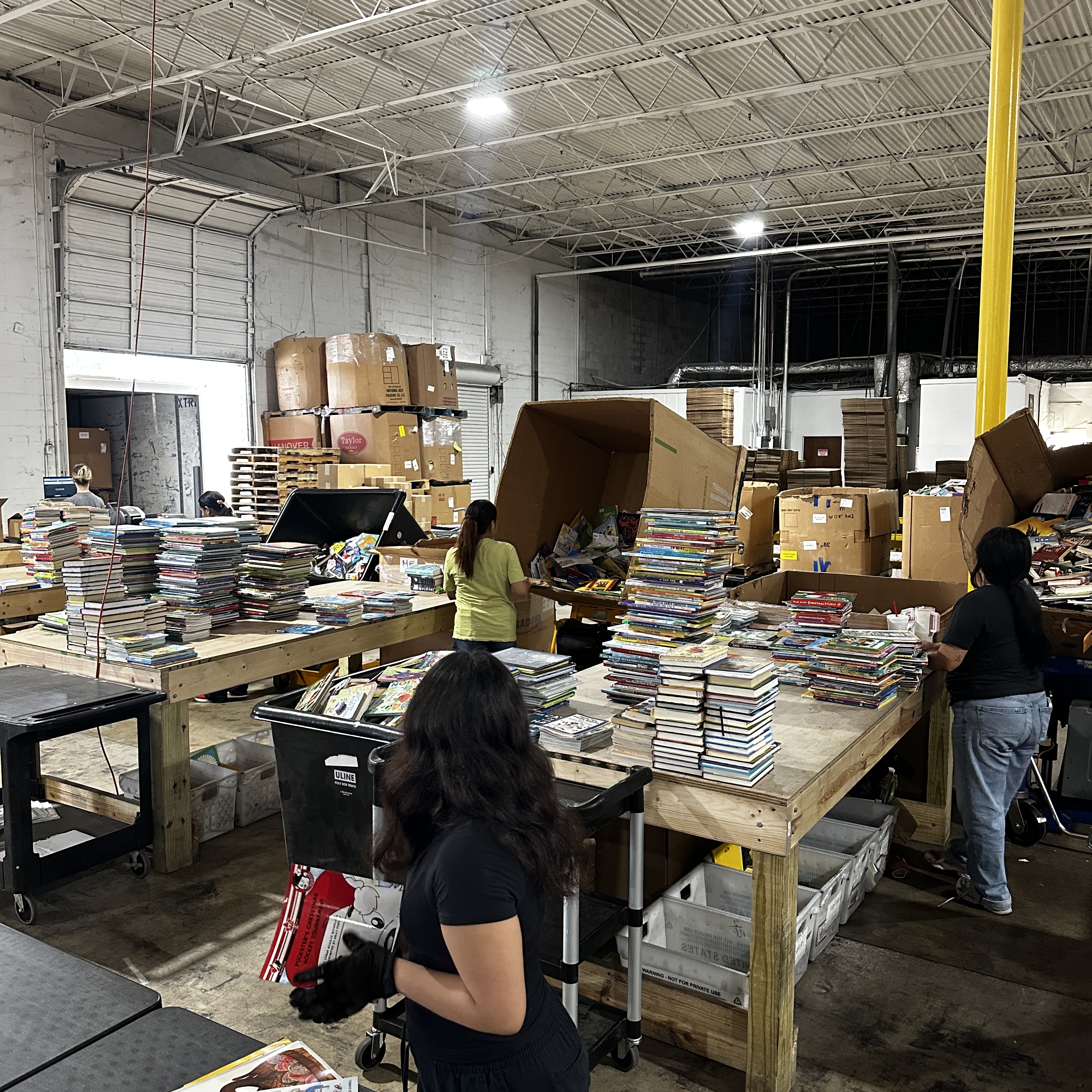 Warehouse or pack table: stacks of childrens books sorted into open boxes and shipping cartons